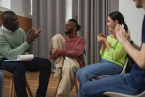 Happy people in group therapy with counselor during ecstasy abuse rehab