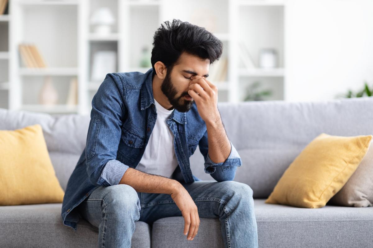 Overcoming Seasonal Depression person sitting on couch struggling with headache while working toward overcoming seasonal depression