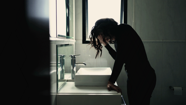 5-Alcohol-Addiction-Symptoms person in dark bathroom standing over sink while struggling with alcohol addiction symptoms