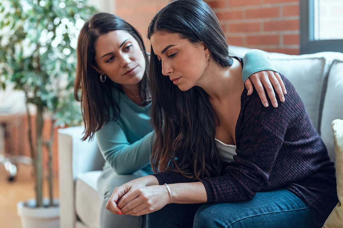 Signs-Of-Polysubstance-Abuse-In-A-Friend person comforting friend while sitting on couch after noticing signs of polysubstance abuse in a friend