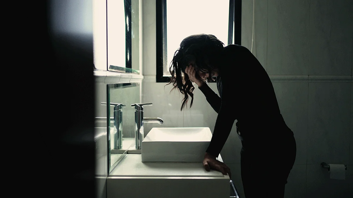 person in dark bathroom standing over sink while struggling with alcohol addiction symptoms