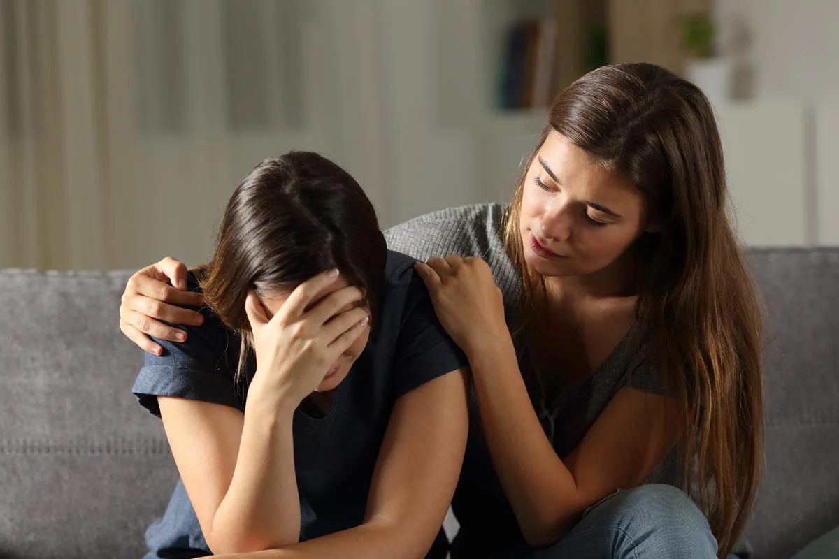 woman on couch consoling another woman experiencing heroin addiction symptoms
