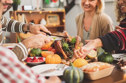 family at the table celebrating sober Thanksgiving as son carves the turkey
