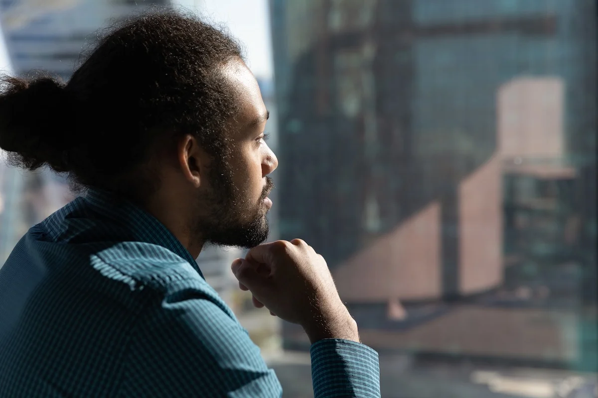 A man sits by a window looking out thoughtfully at a cityscape