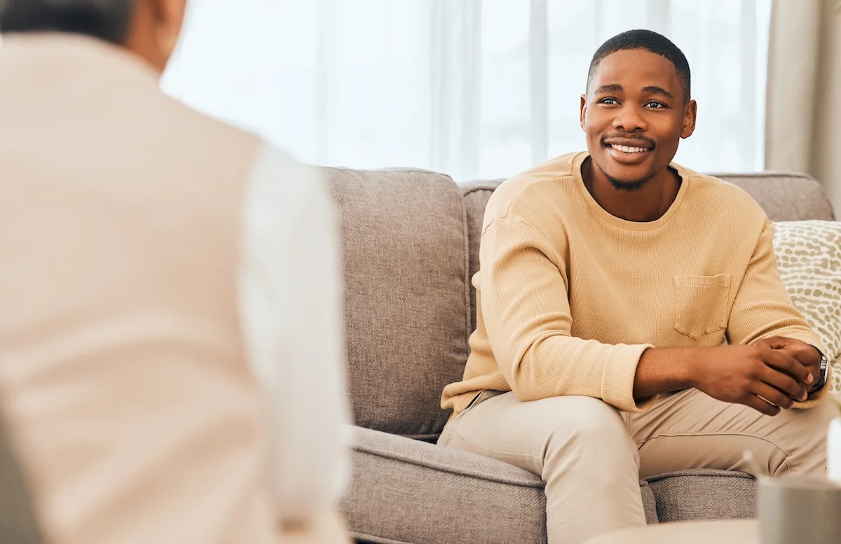 Man smiling while talking with a counselor during a therapy session on a sofa.